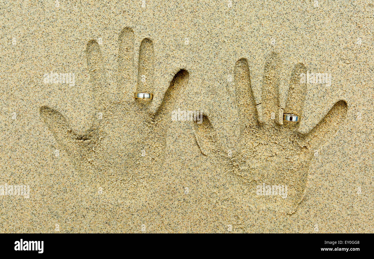 Zwei Handformen in den Sand. Jedes Blatt hat einen goldenen Ehering am vierten Finger. Stockfoto