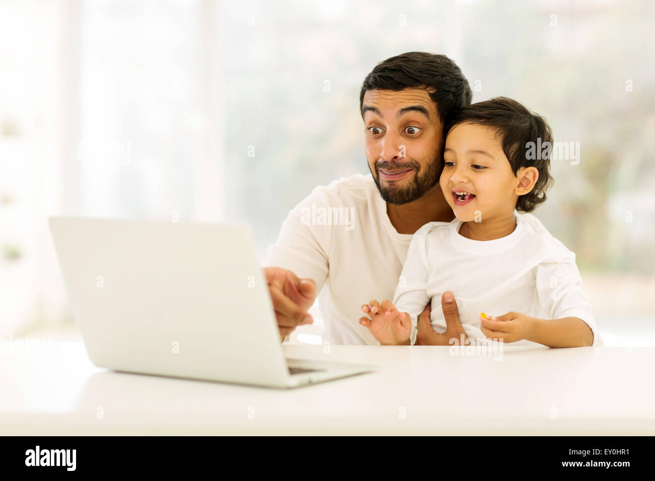 verspielte junge indische Mann mit Laptop mit seinem Sohn zu Hause Stockfoto