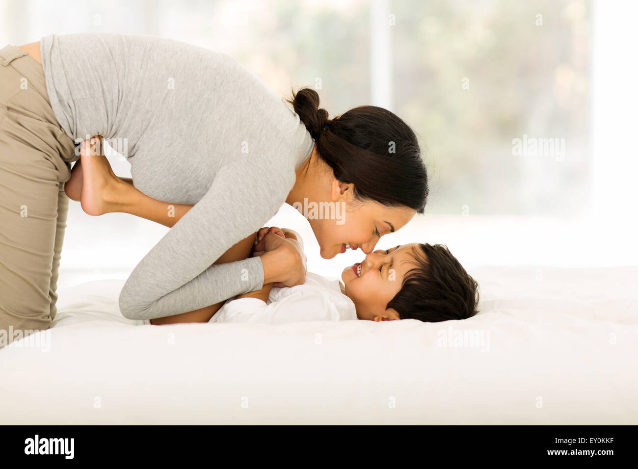 glückliche indische Mutter spielen mit ihren kleinen Jungen auf Bett Stockfoto