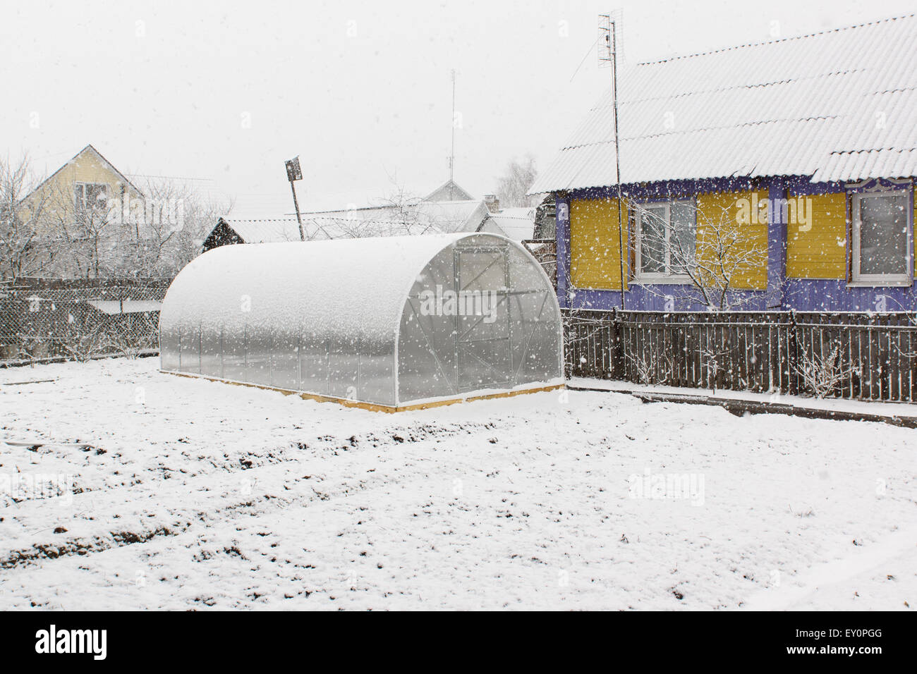 Das Gewächshaus aus Kunststoff befindet sich auf der Erde und fallenden Schneeflocken Stockfoto