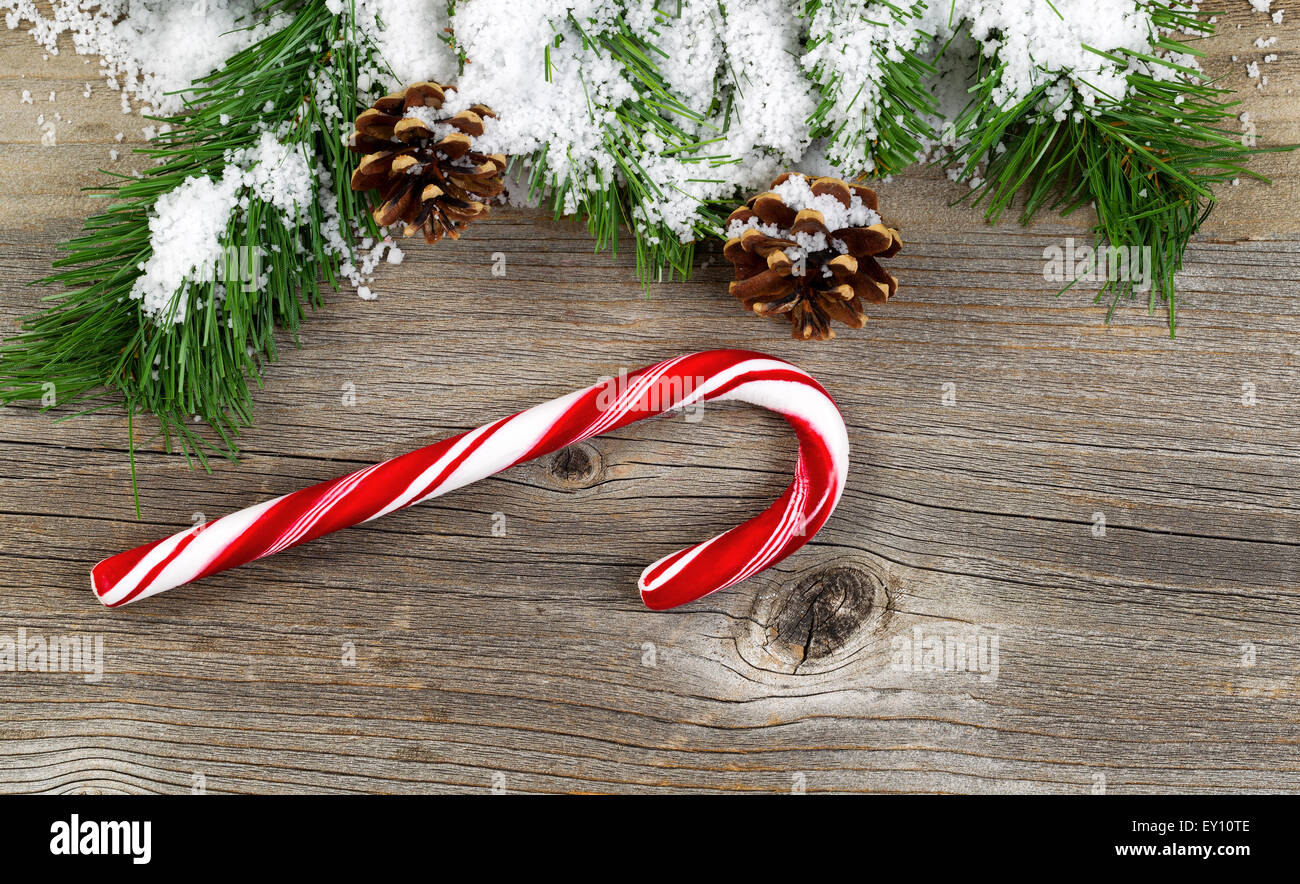 Weihnachten-Grenze mit Schnee bedeckt Baum Tannenzweigen, Zapfen und eine einzelne große Zuckerstange auf urigen Holzbrettern. Stockfoto