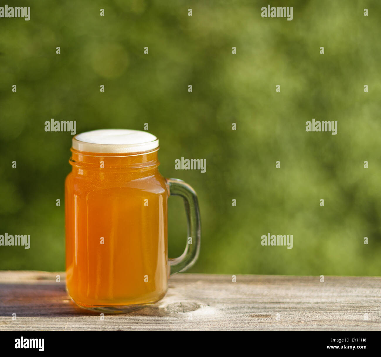 Pint goldene Bier auf rustikalen Holz mit unscharfen, grünen Bäumen im Hintergrund. Frisch gegossen, um die Natur zu genießen. Stockfoto