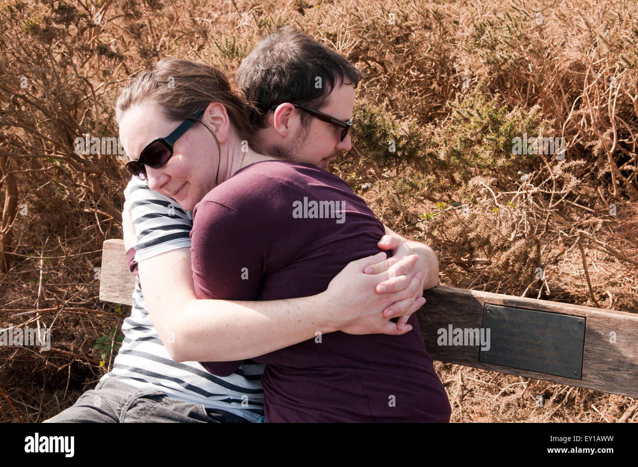 Paar mit ihre Arme umeinander sitzen auf einer Bank Stockfoto