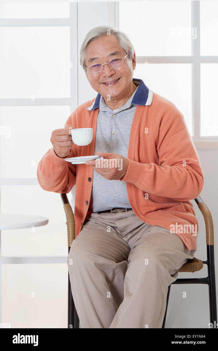 Senior Mann, der eine Tasse trinken und lächelt in die Kamera hält, Stockfoto