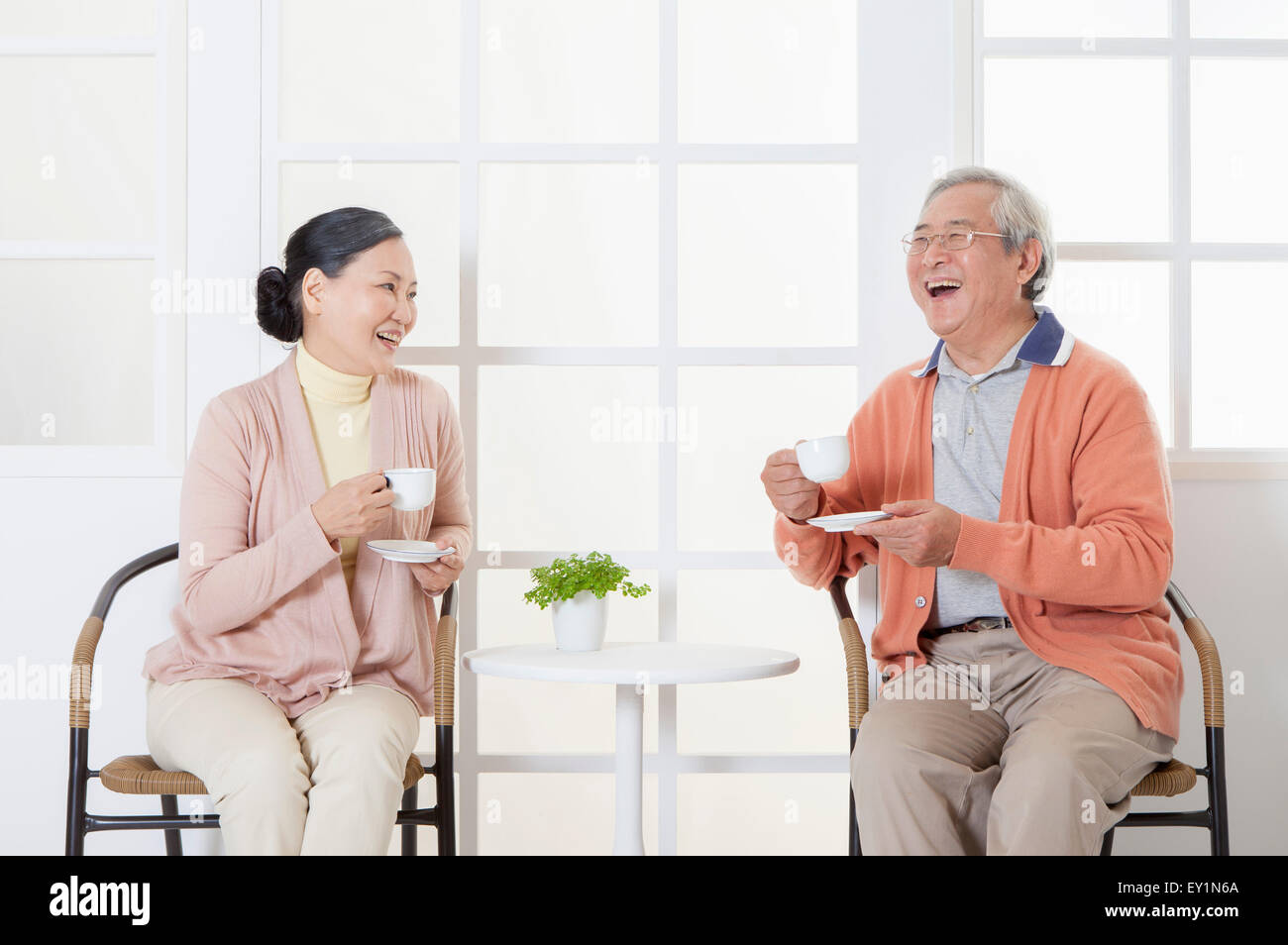 Älteres paar sitzen, hält eine Tasse trinken und lächelt glücklich miteinander, Stockfoto