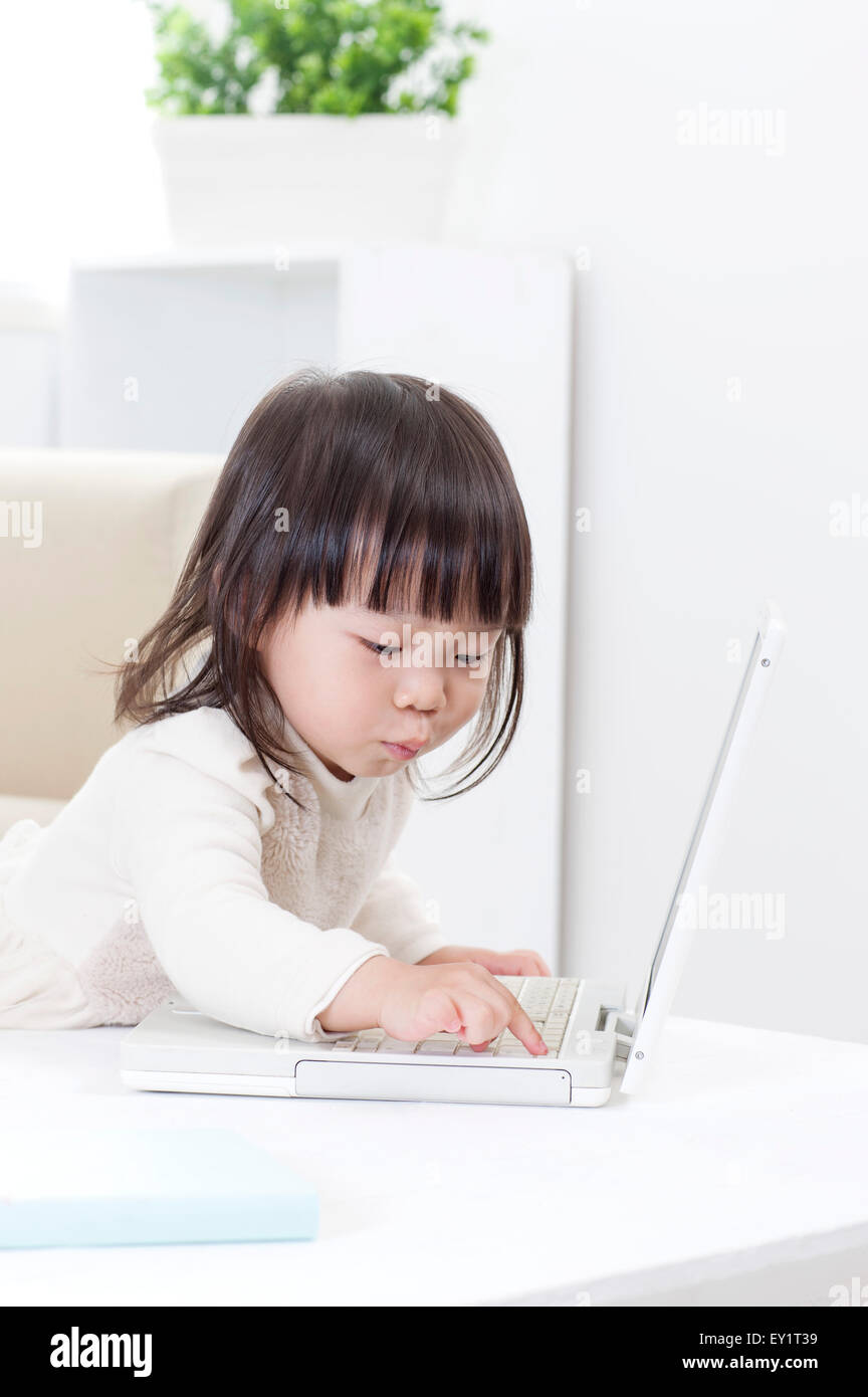 Babymädchen spielen mit Laptop und schaut, Stockfoto
