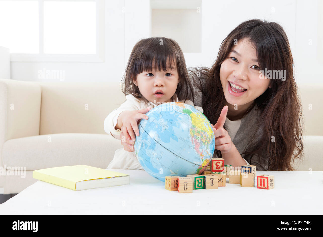 Mutter und Baby Mädchen spielen mit Schreibtisch Globus zusammen und lächelt in die Kamera, Stockfoto