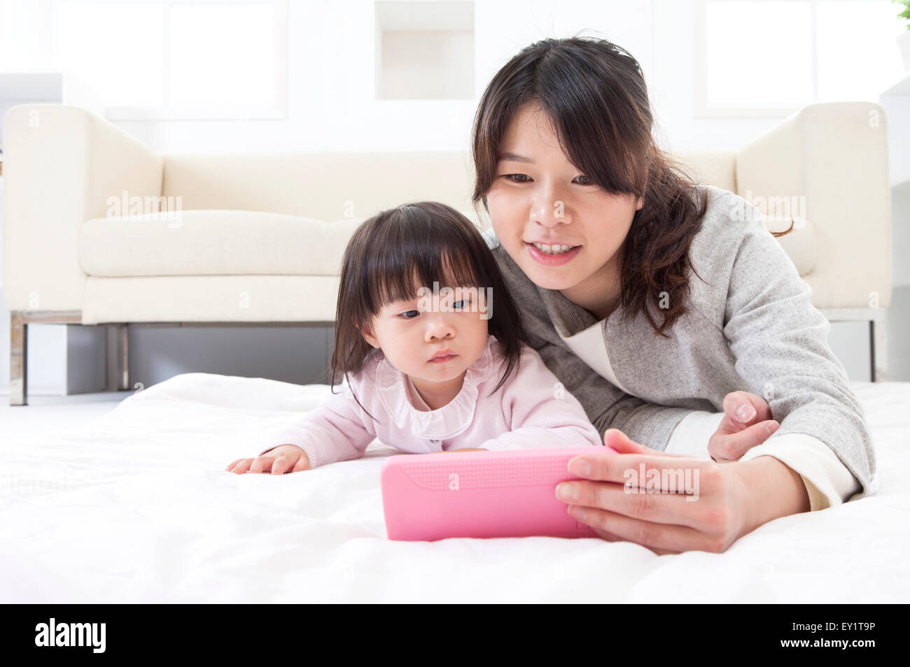 Mutter und Baby Mädchen liegend auf Front und Blick auf Handy zusammen, Stockfoto