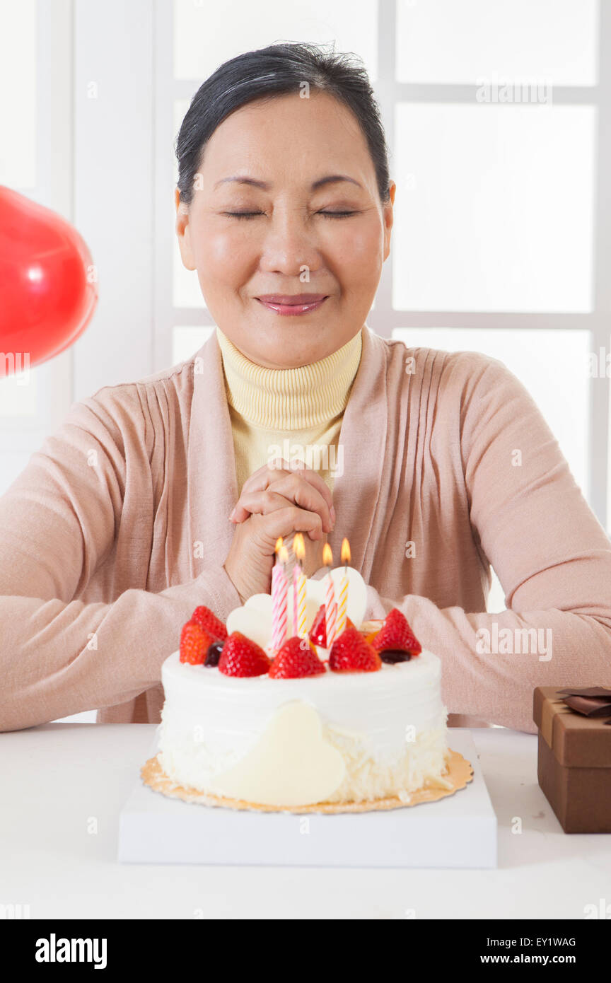 Ältere Frau feiert Geburtstag und wünschen mit Augen geschlossen, Stockfoto