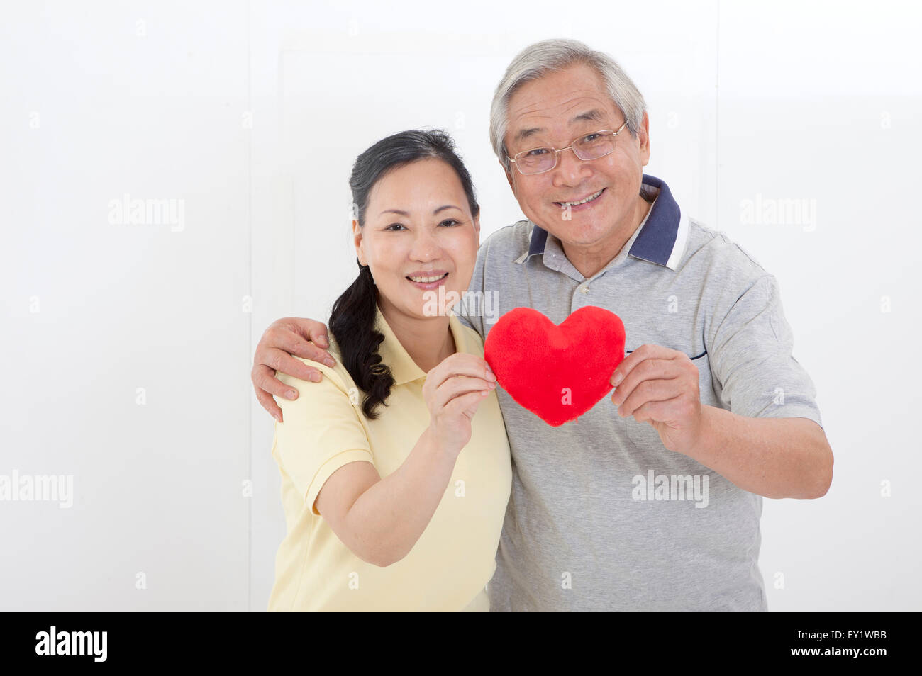 Älteres Paar hält eine Herzform und lächelt in die Kamera, Stockfoto