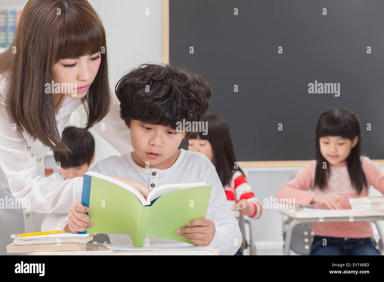 Junge Lehrer und Schüler lesen ein Buch mit Anleitung, Stockfoto