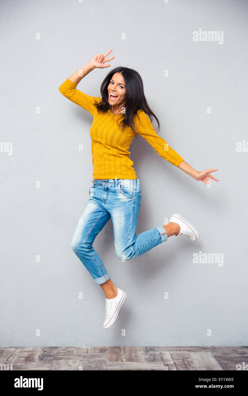 In voller Länge Portrait eine lustige Frau, springen über grauen Hintergrund. Blick in die Kamera Stockfoto