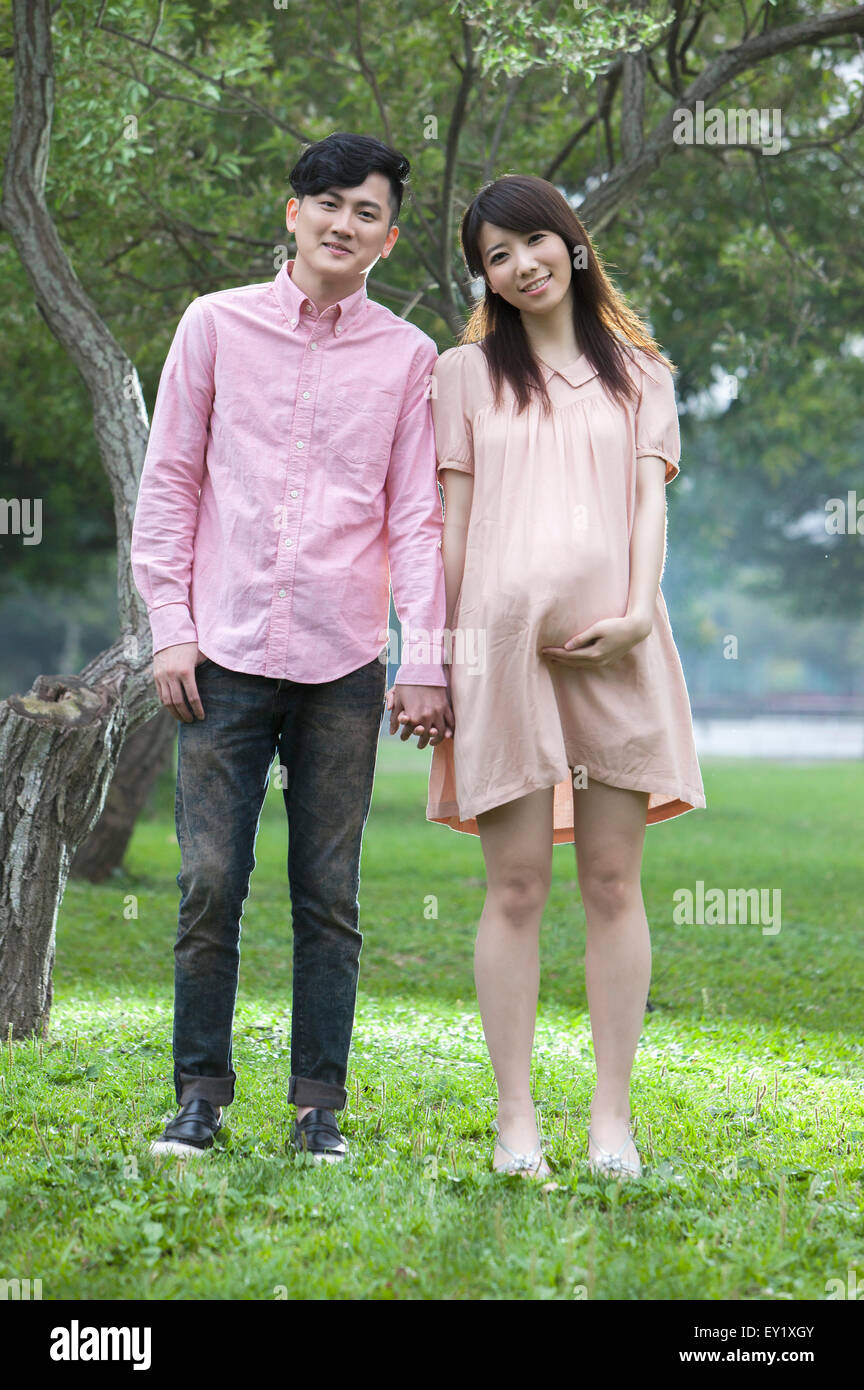 Junger Mann und schwangere Frau auf dem Rasen stehen und Hand in Hand mit Lächeln zusammen, Stockfoto