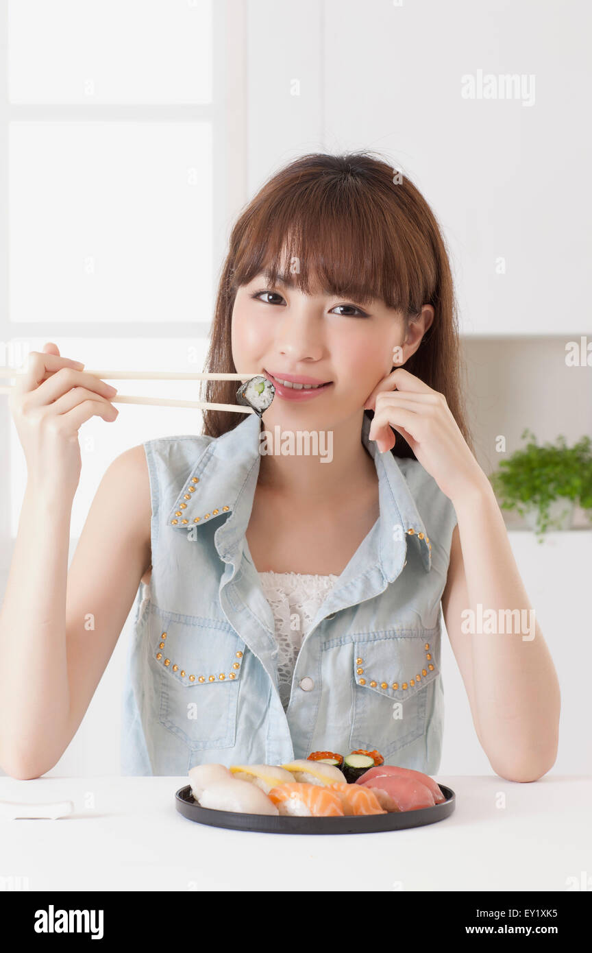 Junge Frau hält Sushi und lächelt in die Kamera, Stockfoto