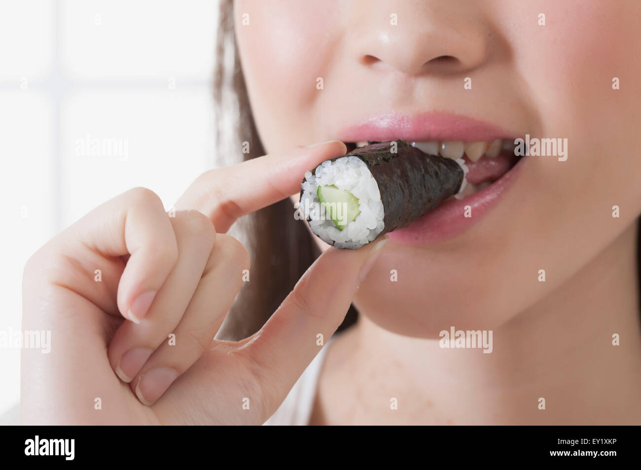 Junge Frau hält Sushi und lächelt in die Kamera, Stockfoto