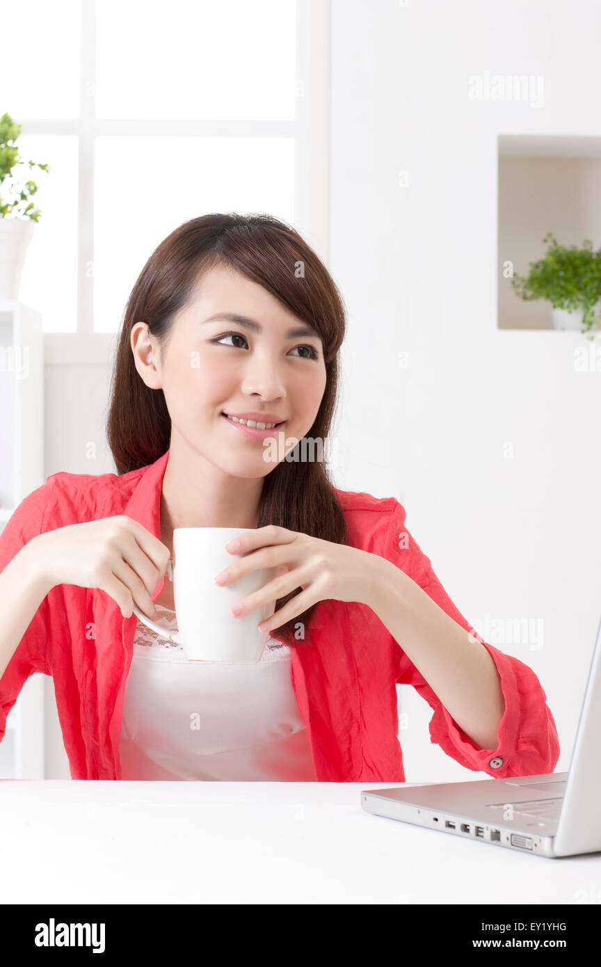 Junge Frau hält eine Kaffeetasse und wegschauen mit Lächeln, Stockfoto
