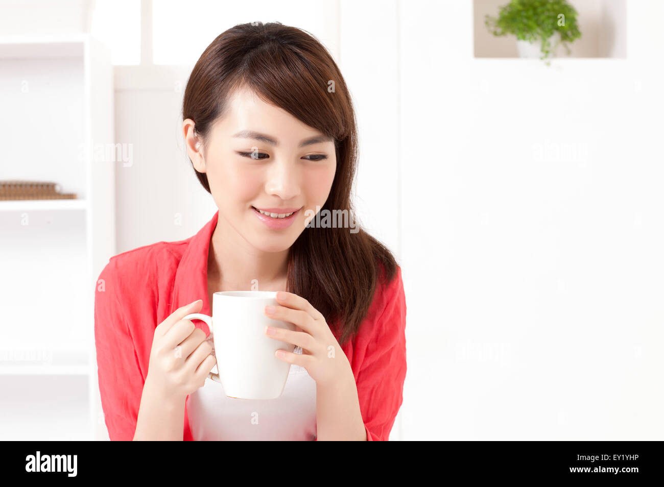 Junge Frau hält eine Kaffeetasse und blickte mit Lächeln, Stockfoto