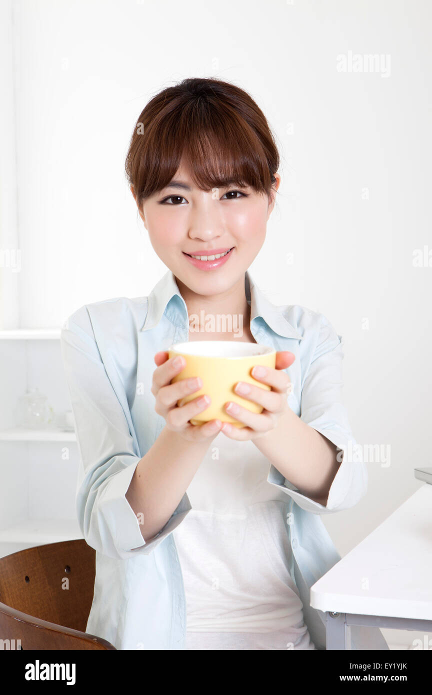 Junge Frau hält eine Kaffeetasse und lächelt in die Kamera, Stockfoto