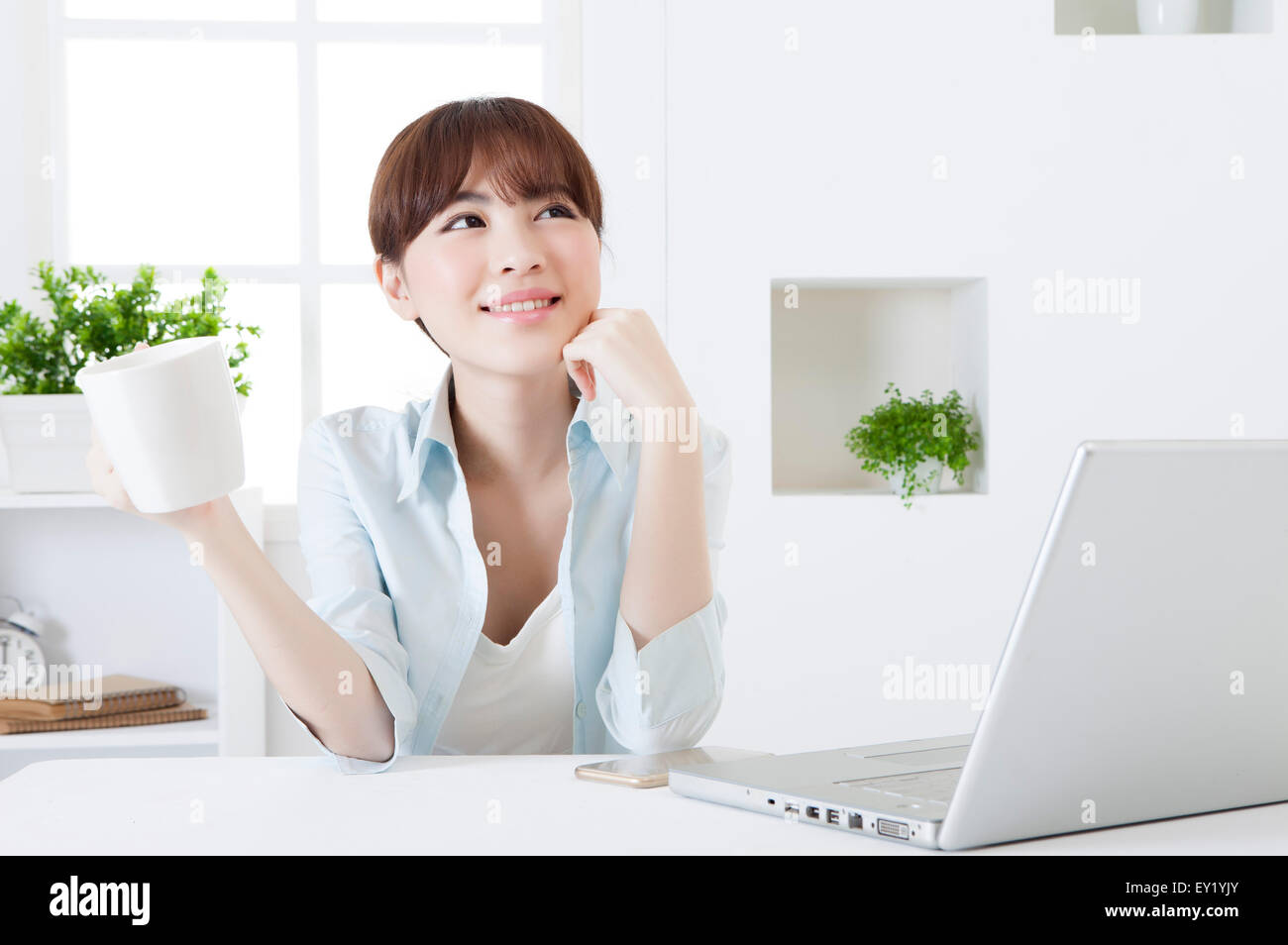 Junge Frau hält eine Kaffeetasse und blickte mit Lächeln, Stockfoto