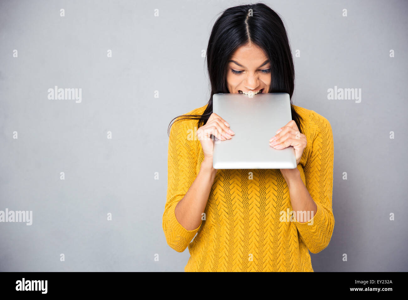 Böse Frau beißen Tablet-Computer auf grauem Hintergrund Stockfoto