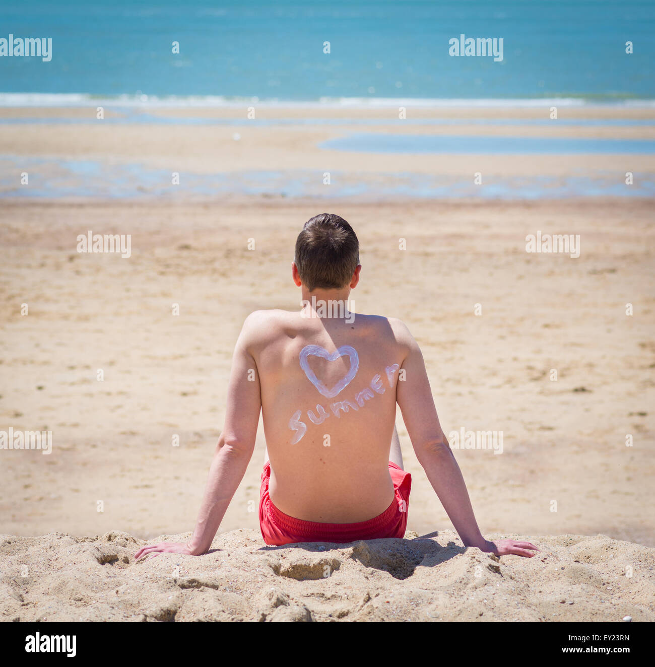 Mann am Strand sitzen und entspannen mit einem Herz auf dem Rücken Stockfoto