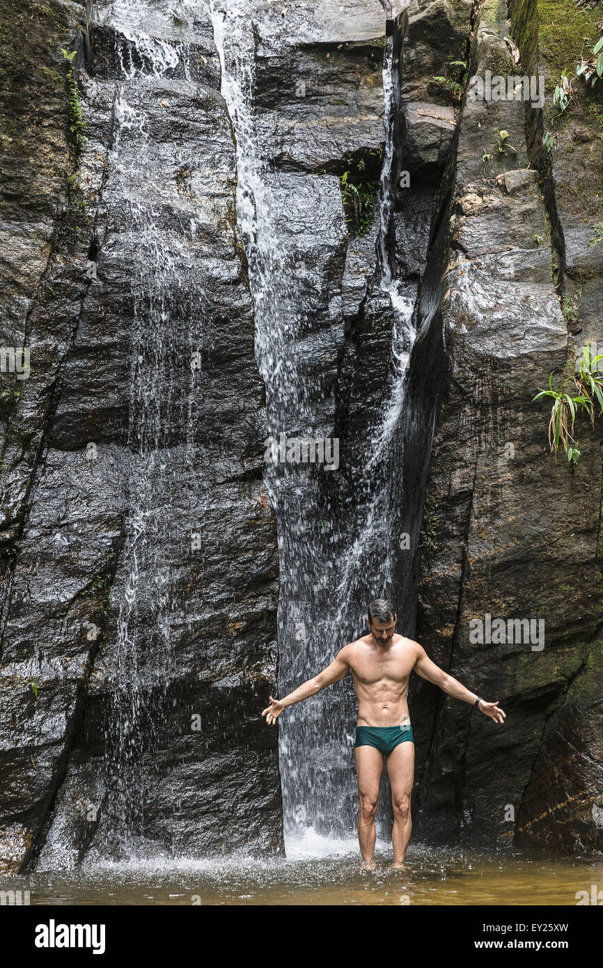 Reifer Mann stehend mit offenen Armen vor Wasserfall, Tijuca Wald, Rio De Janeiro, Brasilien Stockfoto