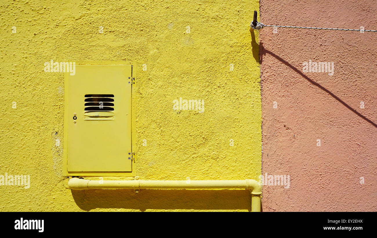 Metallrohr und Elektrokasten auf gelbe Farbe Wand in Burano, Venedig, Italien Stockfoto