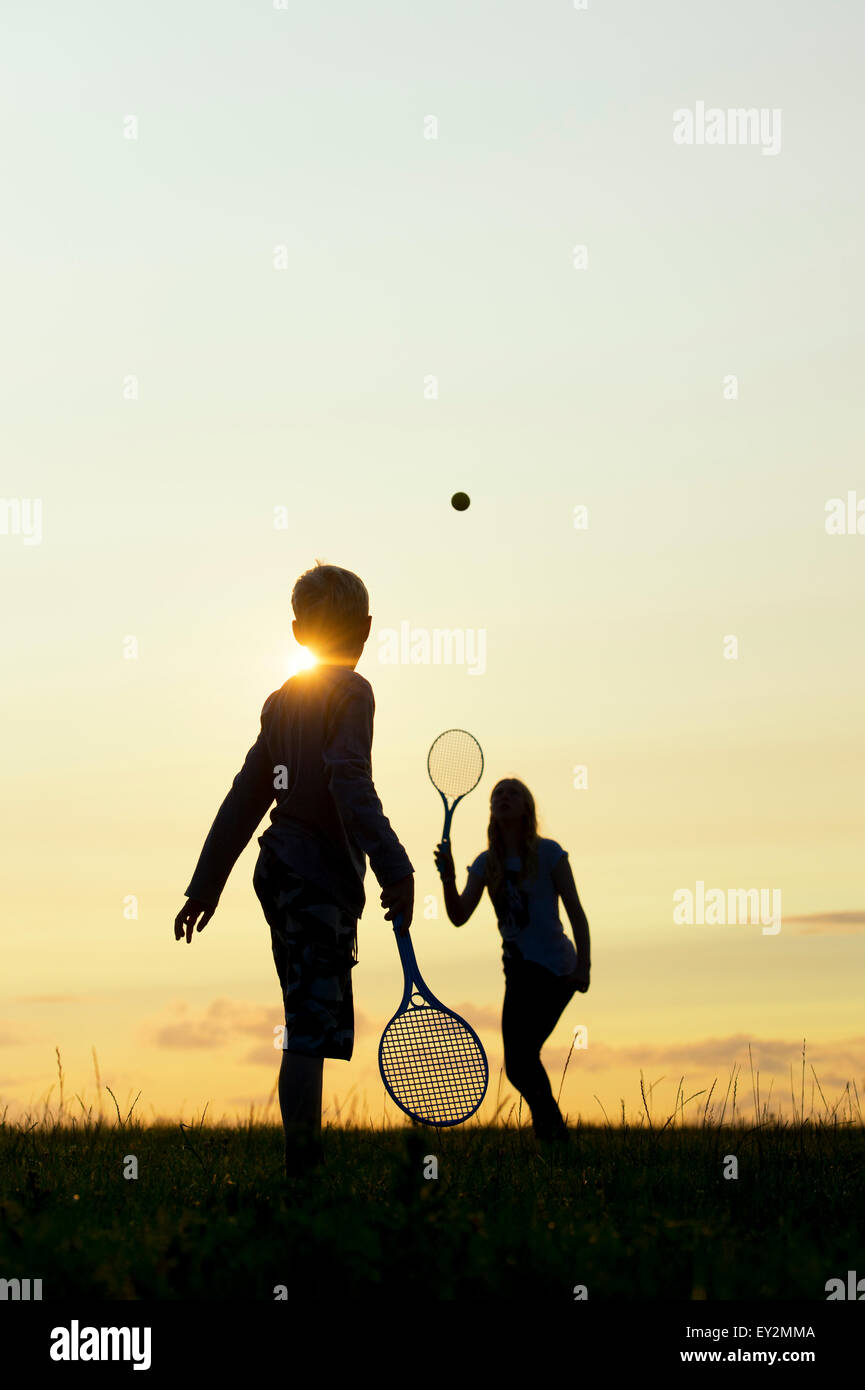 Junge Mädchen und jungen im Sonnenuntergang kurz Tennis zu spielen. Silhouette Stockfoto