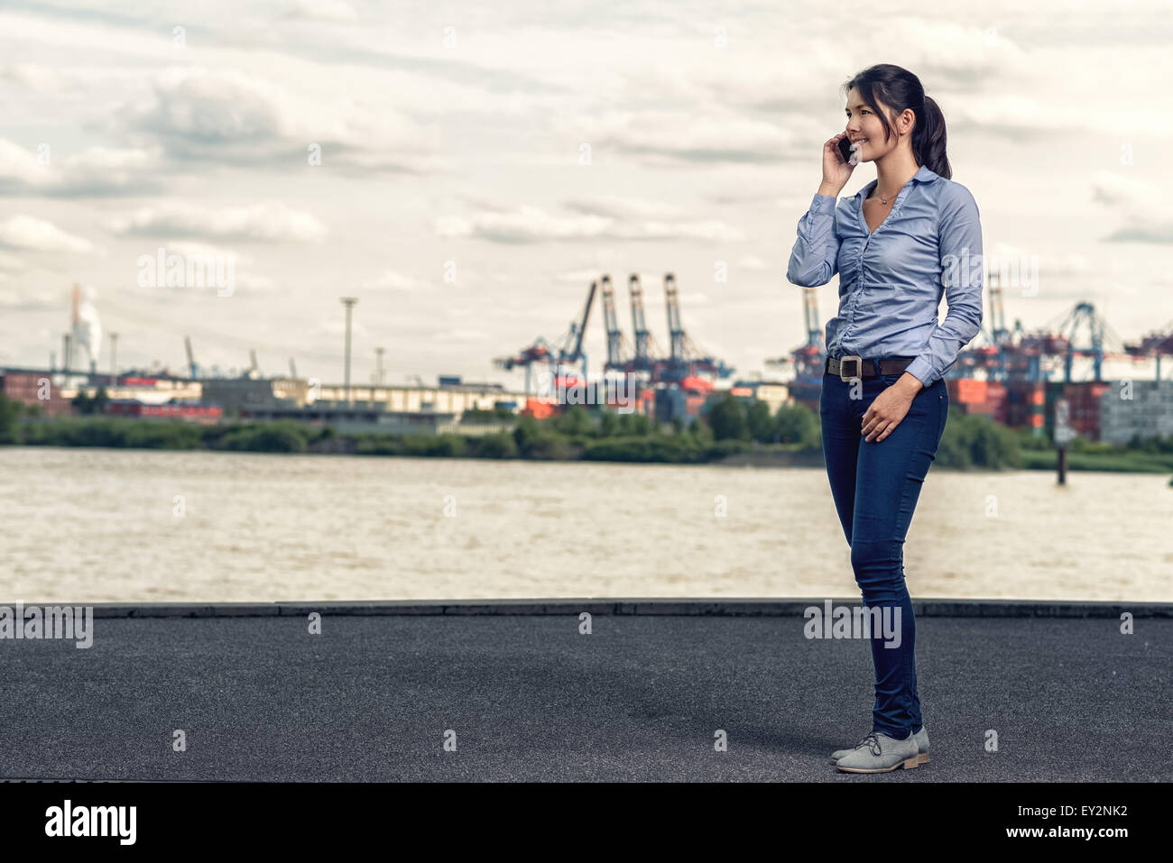 Attraktive Brünette glücklich Frau tragen casual-Outfit als blaue skinny-Jeans und Hemd, beim Telefonieren mit Handy und walking Stockfoto