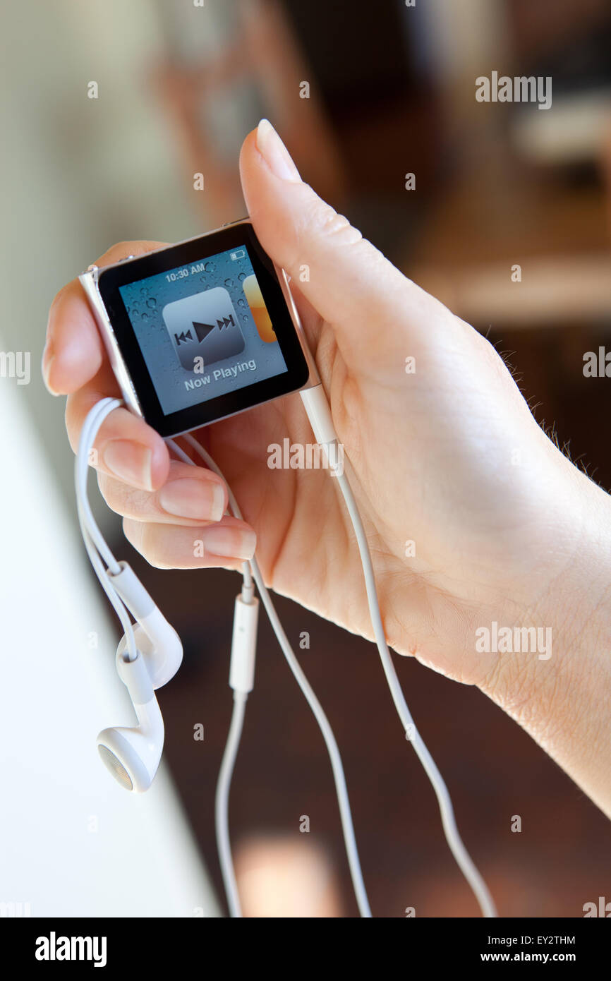 Nahaufnahme von einem Apple iPod Nano mit Kopfhörern, in ein Womans Hand zeigt den aktuellen iTunes Bildschirm gehalten. Stockfoto
