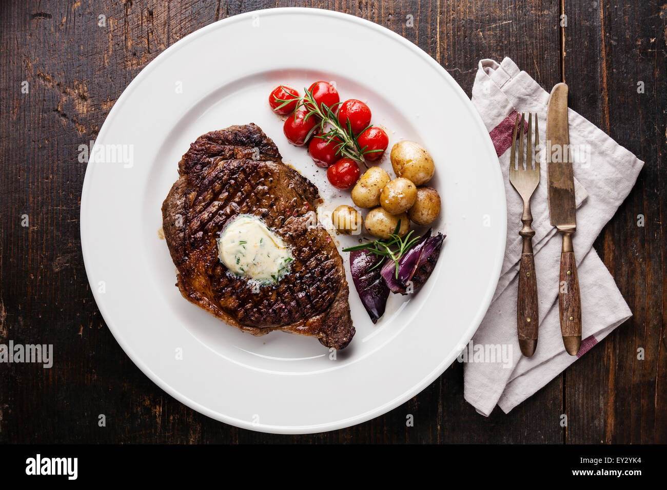 Gegrilltes Steak Entrecote mit Kräuterbutter und Babykartoffeln auf weißen Teller auf hölzernen Hintergrund Stockfoto