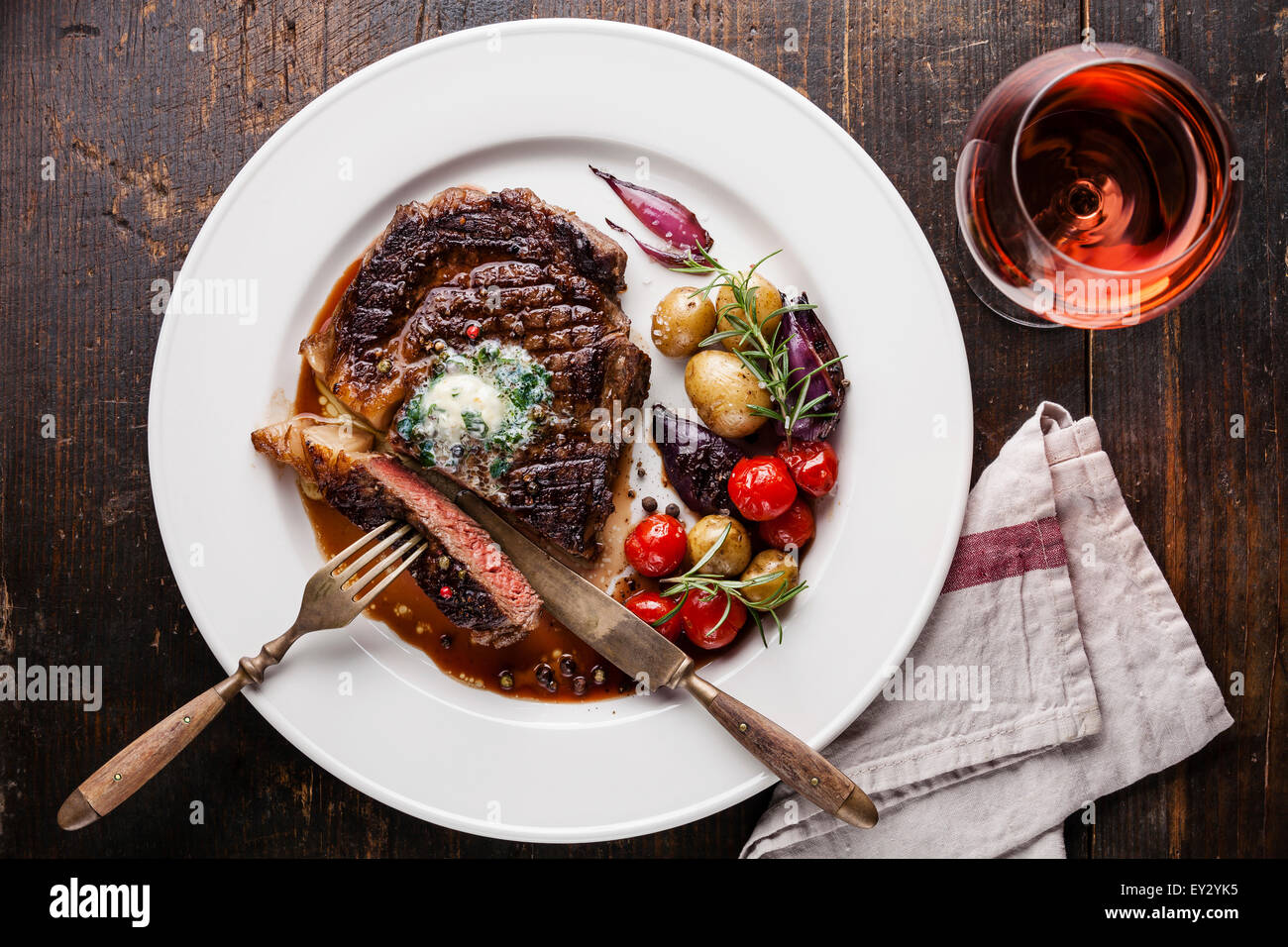 In Scheiben geschnitten mittlere seltene Gegrilltes Beefsteak Ribeye mit Kräuterbutter und Babykartoffeln und Wein auf weißen Teller auf hölzernen Hintergrund Stockfoto