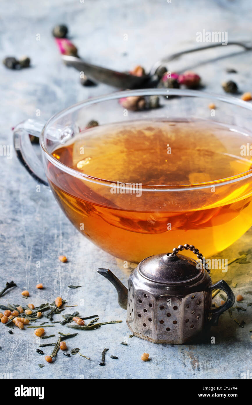 Vintage Teesieb Teekanne und Glas Tasse heißen Tee mit trockenen grünen Teeblätter. Alte Zinn Backgtound. Stockfoto