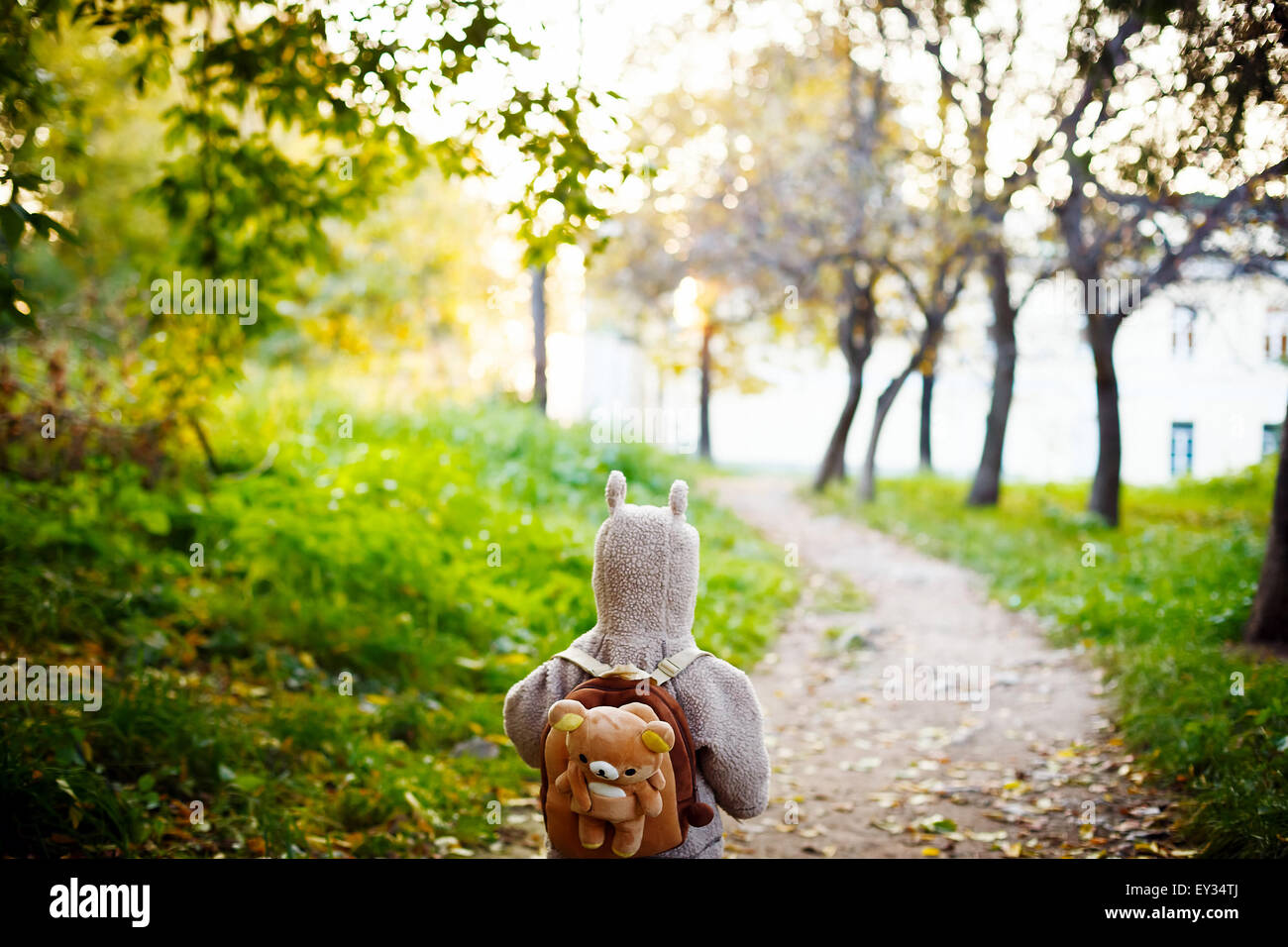 Niedliche Geißlein in lustige Jacke mit tierischen Ohren auf Motorhaube und Teddybär Rucksack Reisen im Park. Ansicht von hinten. Sel Stockfoto