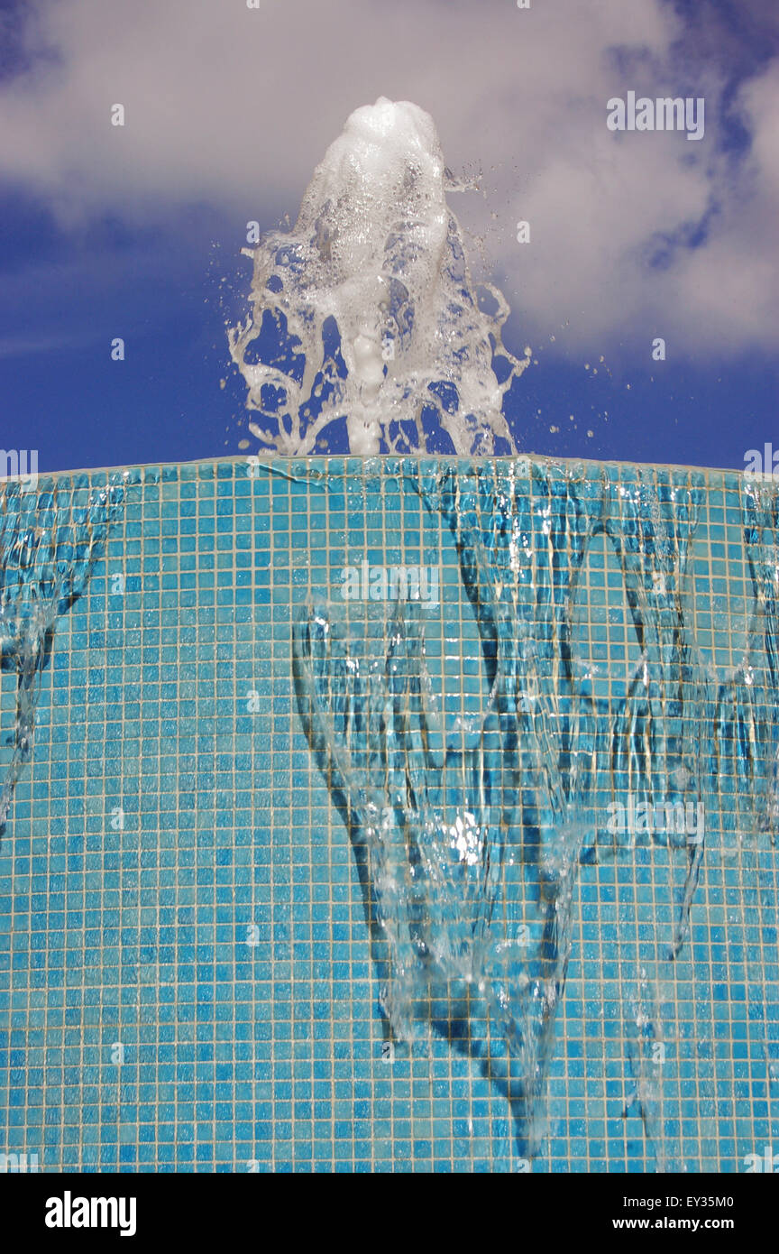 Nahaufnahme eines leichten blau gekachelten Brunnens mit Wasser speienden nach oben gegen einen sonnigen Himmel. Stockfoto