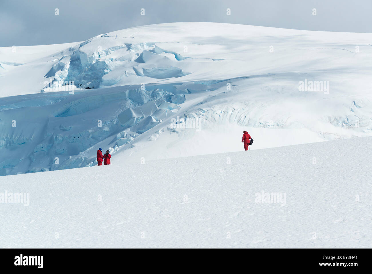 Drei Menschen stehen auf dem Eis vor einem Berg bedeckt in Eis und Schnee. Stockfoto