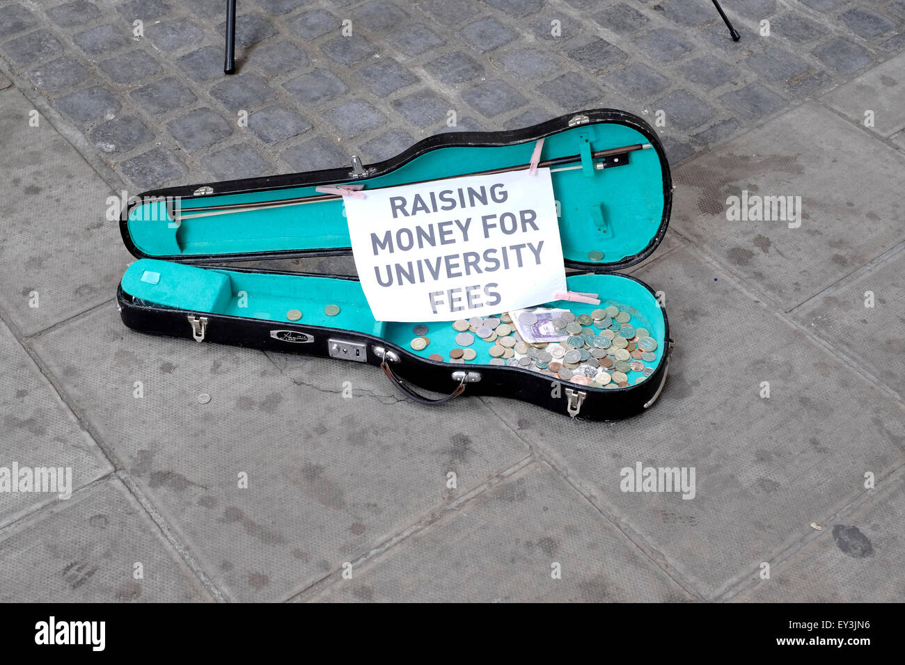Ein Gitarrenkoffer setzen auf einem Bürgersteig mit zwei Straßenmusiker mit ein Zeichen Lesung "Geld für Studiengebühren" Stockfoto
