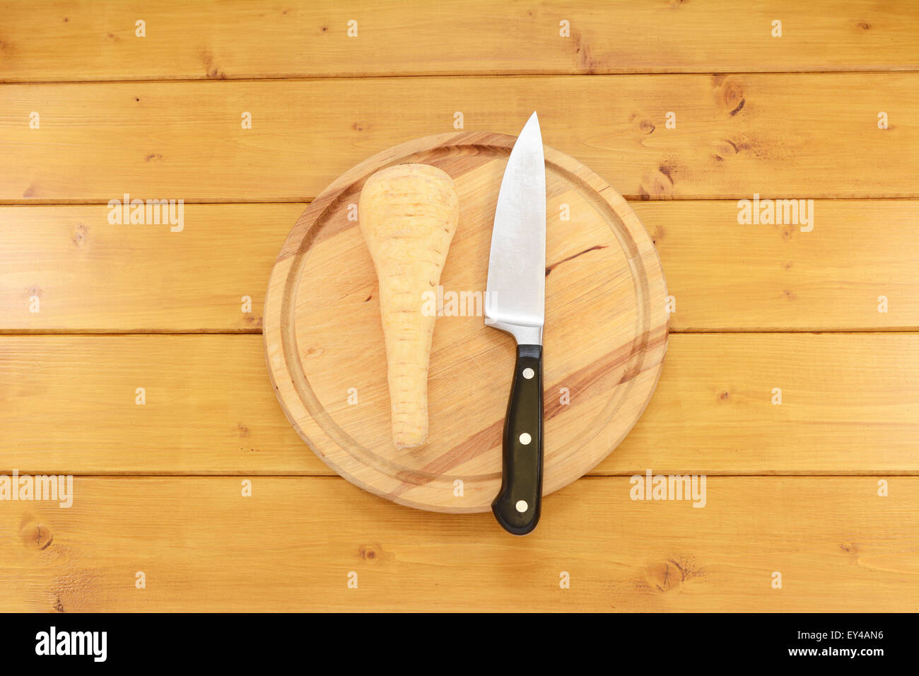 Ganze rohe Pastinake mit einem scharfen Küchenmesser auf einem Holzbrett Stockfoto