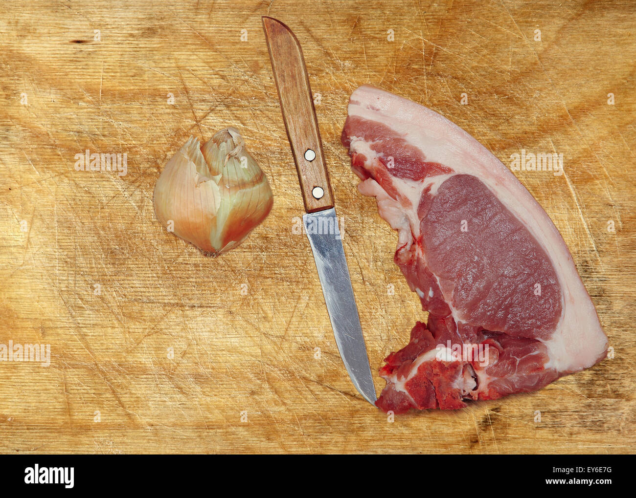 Rohes Schweinefleisch, Messer und Zwiebeln auf Schneidebrett. Stockfoto