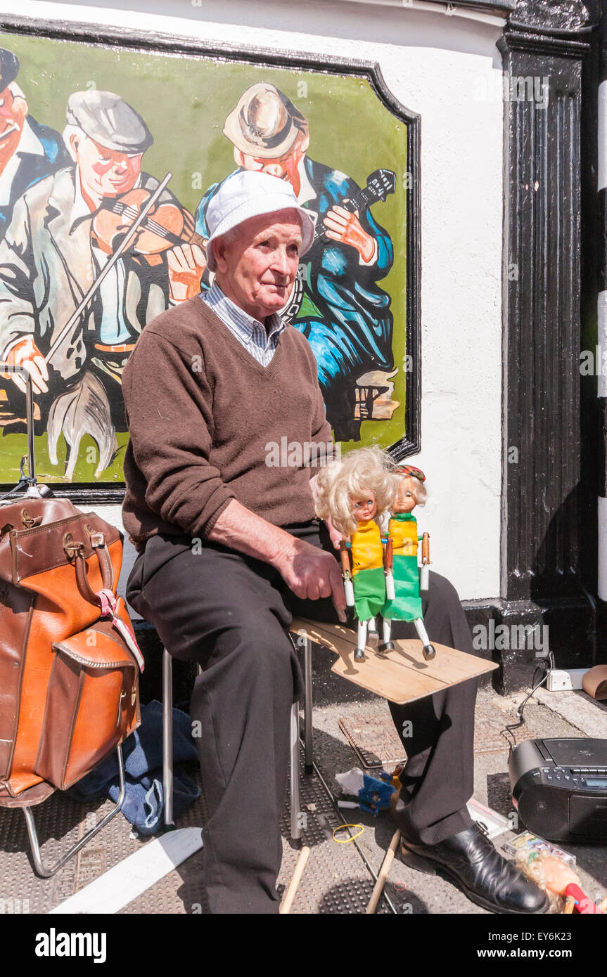 Ein älterer Mann Schnallen wie er Kinder mit tanzenden Puppen unterhält Stockfoto