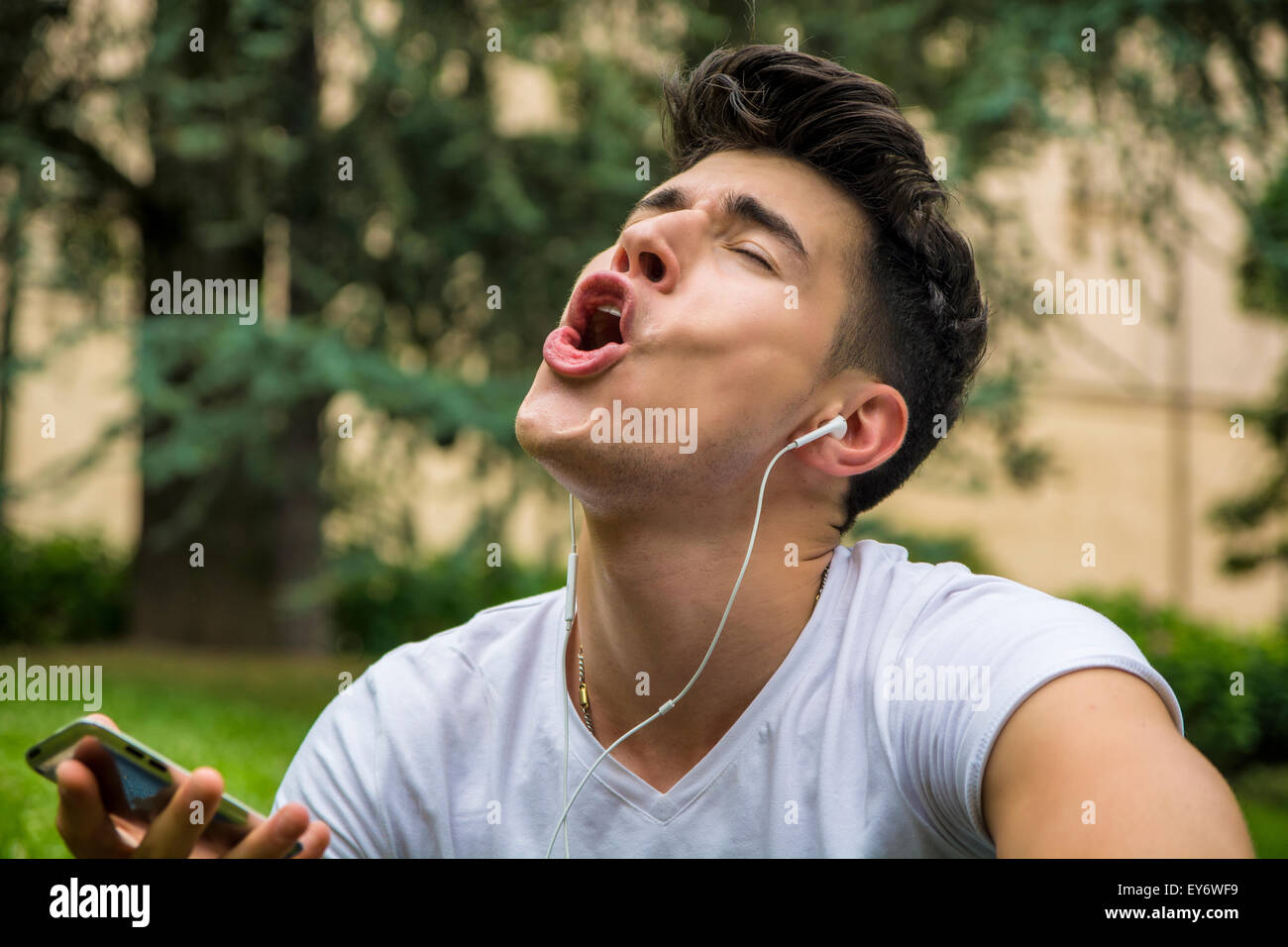 Junge Mann singen Out Loud während hören seine Lieblings Musik mittels Kopfhörer im Park hautnah. Stockfoto