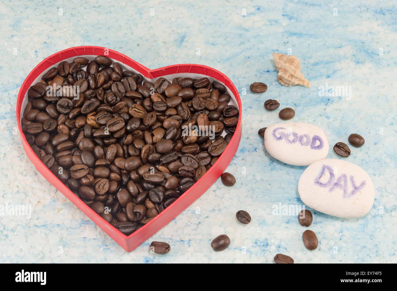 Herzförmige Box gefüllt mit gebratenen Kaffeebohnen auf blauem Hintergrund mit einem "guten Tag" Stockfoto