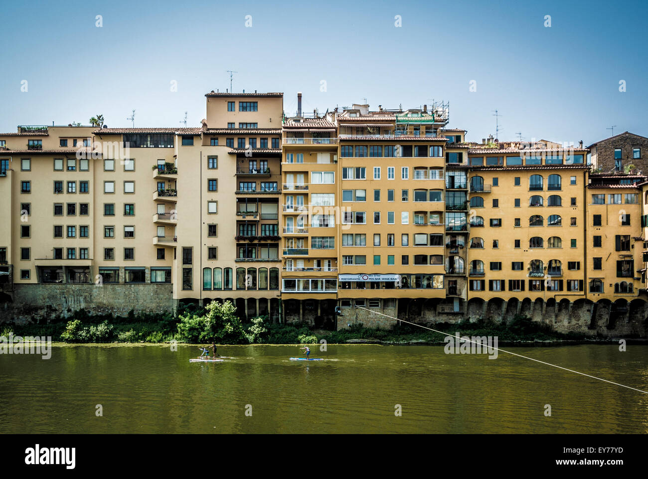 Moderne Florentiner am Flussufer Gebäude mit zwei aufstehen Surfer paddeln auf dem Fluss Arno, Florenz, Italien. Stockfoto