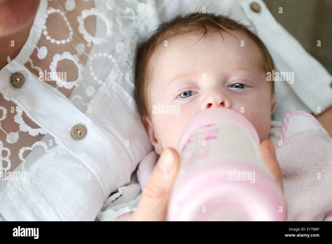 Eine sehr junge Babys Milch aus der Flasche gefüttert zu werden. Die Muttergesellschaft hält es einen Winkel mit dem Baby auf dem Rücken und in den Armen liegen und Fütterung Stockfoto