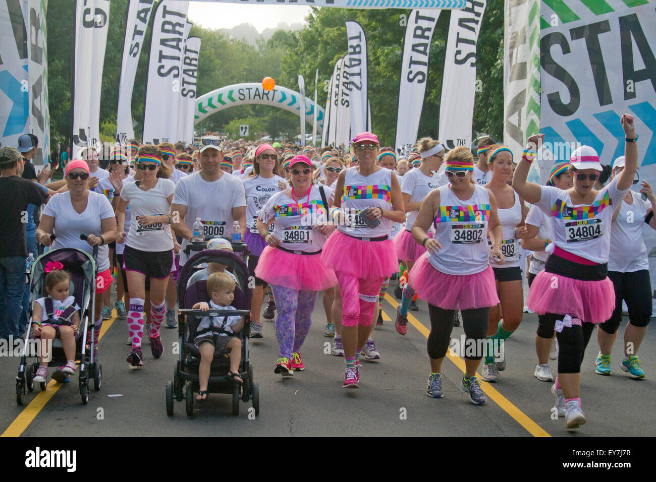 Glückliche Farbe laufen Läufer tragen bunte Tutus und Stirnbänder und Kinderwagen platzen begeistert von der Startlinie Stockfoto