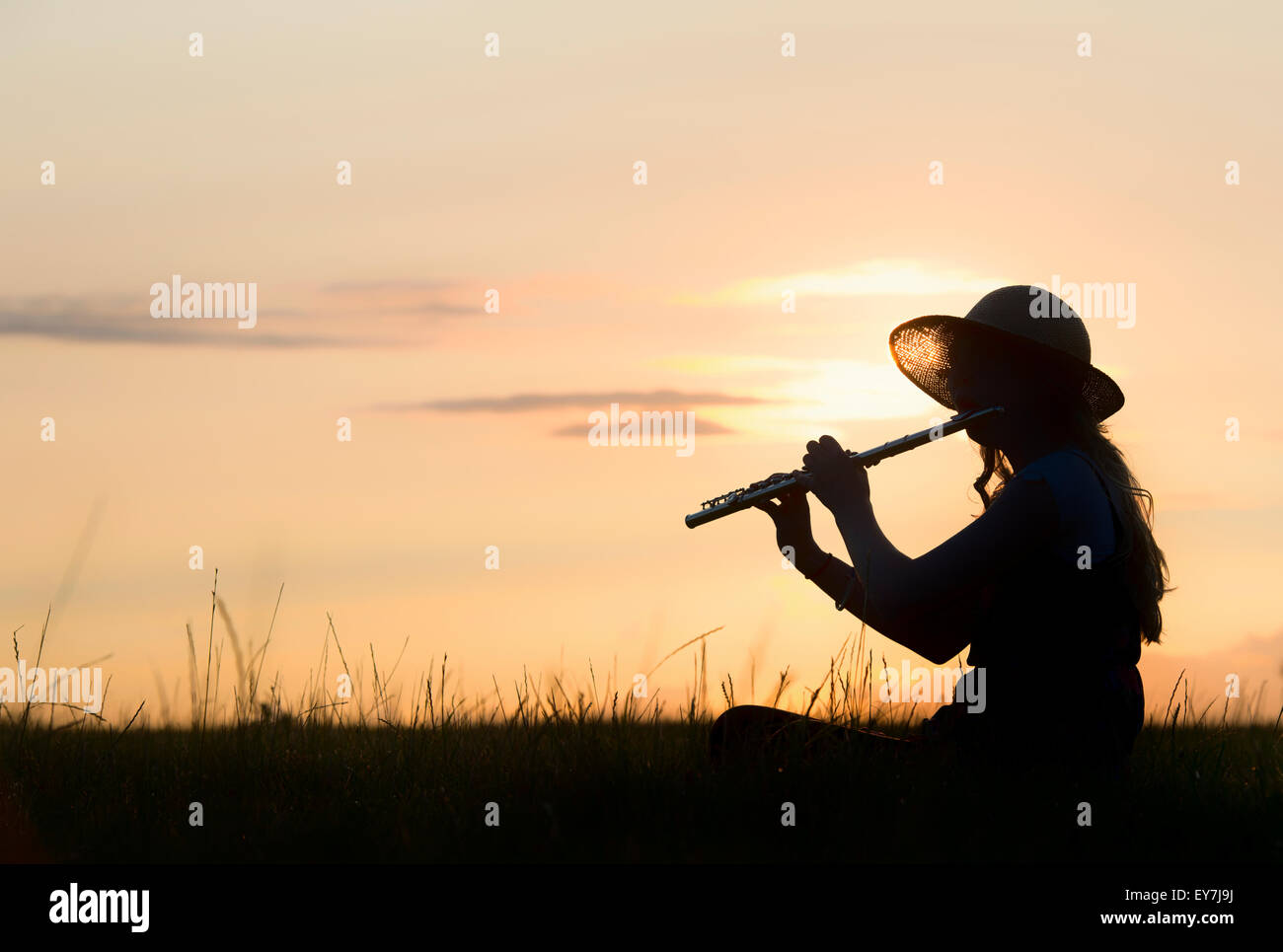 Teenager-Mädchen saß auf dem Rasen ein Flötenspiel bei Sonnenuntergang. Silhouette Stockfoto