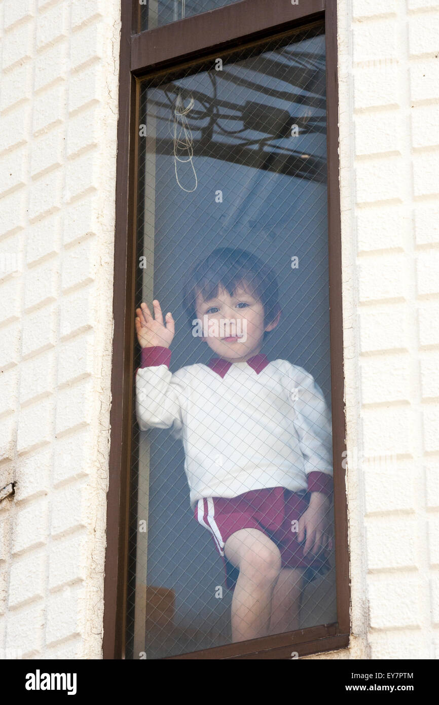 Kind, Junge, 3-4 Jahre alt, an der oberen Fenster in voller Länge ansehen in Sport Shorts und Sweat Shirt, an Ansehen und winkte. Stockfoto