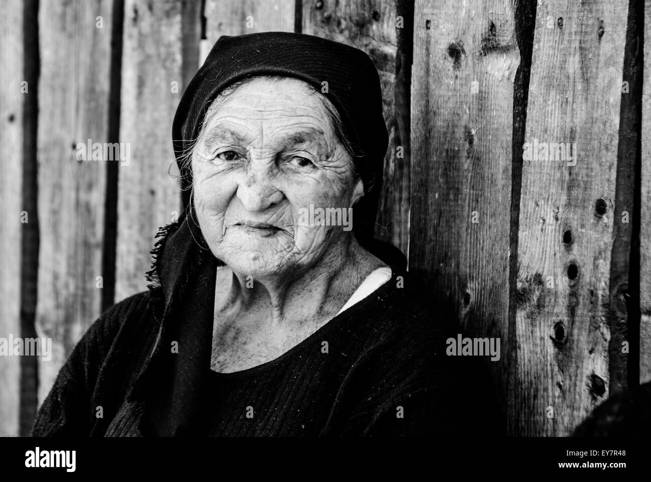Ältere Frauen in traditionellen Kopftüchern lächeln bei Tageslicht vor rustikaler Holzkulisse Stockfoto