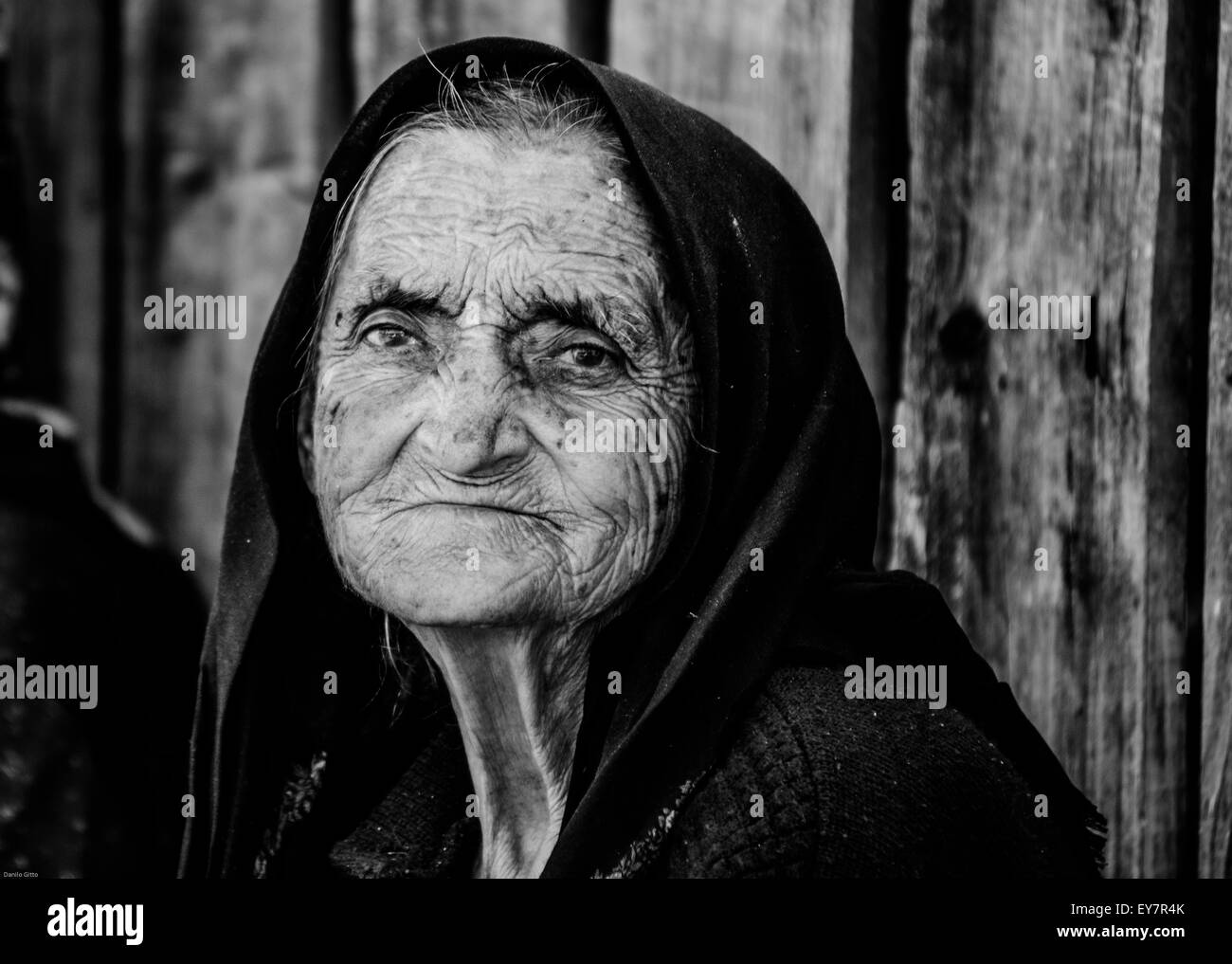 Ältere Frauen in traditionellen Kopftüchern lächeln bei Tageslicht vor rustikaler Holzkulisse Stockfoto