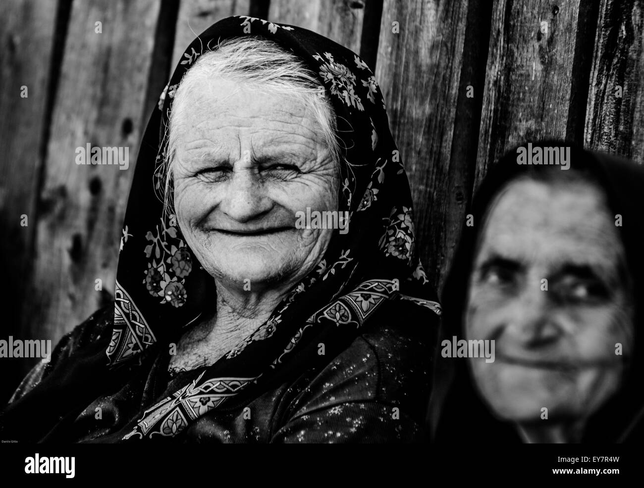 Ältere Frauen in traditionellen Kopftüchern lächeln bei Tageslicht vor rustikaler Holzkulisse Stockfoto